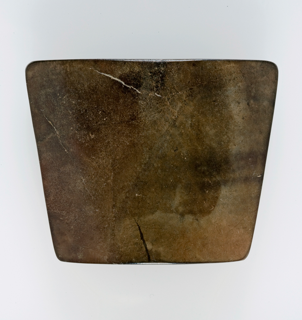 An image of Dark brown jade with black staining, carved in approximately trapezoidal shape. Three joined holes on the top for attachment to the scabbard. Undecorated smooth surface. Nephrite, length, 5.5 cm, width, 4.5 cm, circa 400-1 B.C. Chinese.