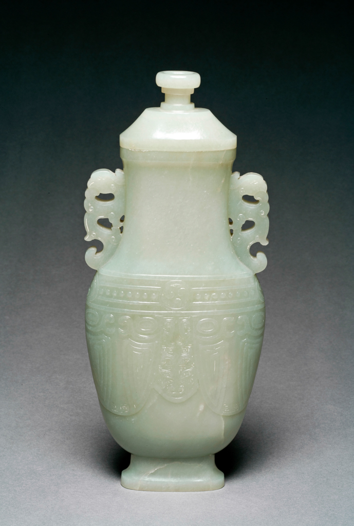 An image of Vase. Pale green jade flattened baluster jade vase, the body decorated with an archaistic taotie face between two cicada. The neck set with phoenix handles and a band of roundels and beads decorated below. nephrite, height, with lid, 24.7 cm, width 11 cm, 1750-1800. Chinese.