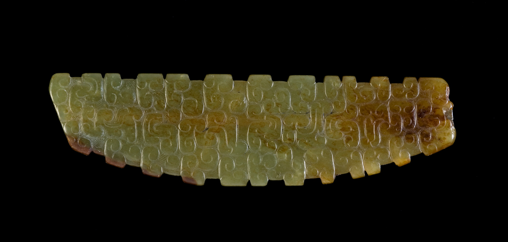 An image of Ornament/Pendant. Pale green translucent jade with brown inclusions, decorated with raised scrolls. A central perforation drilled from both ends for suspension. Nephrite, height, width, 600-400 B.C. Chinese.