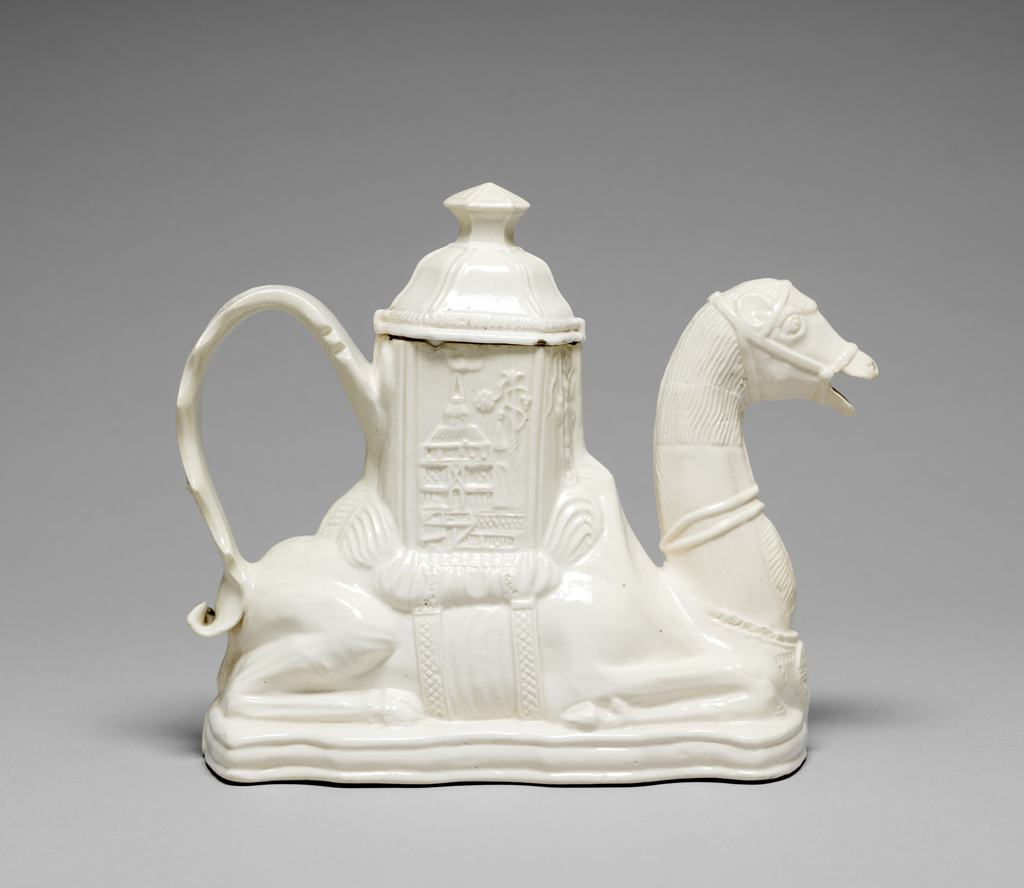 An image of Camel Teapot. Staffordshire, nearlydone (uncertain). In the fom of a camel crouching on a shaped base, with on its back, a tall hexagornal erection secured by two girths. The camel's neck and head with open mouth forms the spout. The loop handle is formed of a flat scalloped band with impressed foliage and flowers. In the panels on the upper part there are Chinese figures and buildings. The domed hexagonal cover has raised lines between its panels, a narrow ribbed border, and a hexagonal slightly conical knob with waisted sides. White salt-glazed stoneware, slip cast, height, whole, 15.5 cm, length, whole, 18.1 cm, circa 1750-1755. English. Rococo.