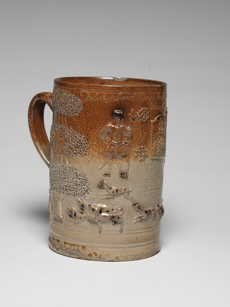 An image of Hunting Mug. Vauxhall Pottery. Decorated with a hare hunt, an inn sign of Queen Ann between Beefeaters, Boscobel Oaks each harbouring a head of future Charles II, and inscription, ‘Drink about Boys to the Pious Memory of Queen Ann/Mary Bayley/1730’. Grey-buff/brown stoneware, thrown and turned, with applied moulded reliefs, hand-modelled trees, and incised decoration and inscription, height, whole, 21.5 cm, width, whole, 29 cm, 1730. London. English.