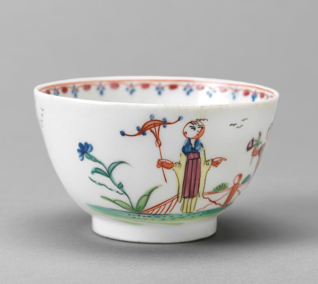 An image of Tea bowl and saucer/cup and saucer. New Hall Porcelain Factory, Staffordshire. Chinoiserie scenes. Pattern no. 20. The circular cup has deep curved sides and stands on a footring. The saucer has deep curved sides and stands on a footring. The cup is decorated on one side with a lady holding a parasol and a boy walking towards her holding a windmill and a flower with a fence behind them. On the right there is a plant in a pot and a small pine bush, and on the left a plant with a blue flower. On the other side there is a mound of grasses and five birds in the sky. Inside the rim is a border comprising a red line, a mauve scalloped line with blue flowers on the points and a dark pink spots on the curves. In the middle there is a small green plant with a purple bud. The saucer is decorated inside with the same figures and flanking motifs on a larger scale, and has a matching border round the rim. Hybrid hard-paste porcelain painted overglaze in blue, two-shades of green, yellow, red, dark pink, pinkish-purple, and black enamels (polychrome). Height, cup, 4.8 cm, diameter, cup, 8.1 cm, height, saucer, 3.4 cm, diameter, saucer, 13 cm, circa 1785-1800. Chinoiserie.
