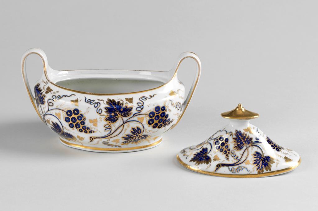 An image of Sugar basin and cover/sugar bowl and cover. New Hall Porcelain Factory, Staffordshire, New Hall. Painted underglaze in mazarine blue with vine leaves, bunches of grapes and tendrils, and gilded. Pattern no. ‘631’ painted in red. Oval with curved sides, and two strap handles which rise upwards before descending to join the lower part of the sides. Inside the top there is a ledge to support the cover. The oval cover rises steeply to the middle where there is a hole, covered by the oval conical knob. The sides of the bowl are decorated with pattern 631 comprising sprays of vine leaves, tendrils and bunches of grapes, and there are gold bands round the lower edge, the top, and the sides of the handles, which also have a longitudinal gold stripe. The cover is decorated en suite but with smaller sprays. It has a wide gold band round the edge and gold knob. Hard-paste porcelain moulded and painted under presumed lead-glaze in mazarine blue and gilded. Transfer-printed underglaze in cobalt blue, height, whole, 12.1 cm, length, whole, 18.8 cm, width, whole, 10.6 cm, circa 1800-1812.