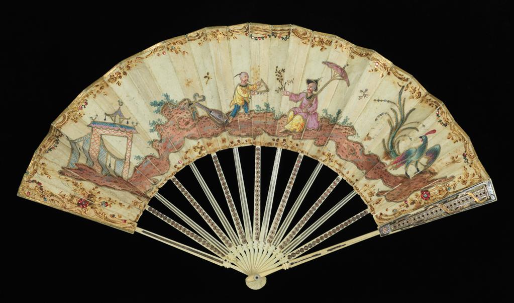 An image of Folding fan. Production Place: England and France. On the silk obverse is a chinoiserie figurative scene painted in gouache and gold paint and decorated with gilt-thread tambour-work outlining, stitched coloured-metal sequins (blue and yellow) and adhered coloured metal foil (red and blue) paillettes. The top edge and sides of the leaf are edged with applied gilt paper. Decoratively-carved sticks and guards of elephant ivory, overlaid with silver part-coloured by tinted lacquer; the ring-and dot motifs on the obverse sticks inlaid with red metal foil. Paper, previously silvered(?), is adhered to the reverse of alternate sticks. The sticks are united with a copper alloy rivet and mother-of-pearl spacers. Silk, backed with paper, length, guards, 27.5 cm, circa 1780. Chinoiserie.