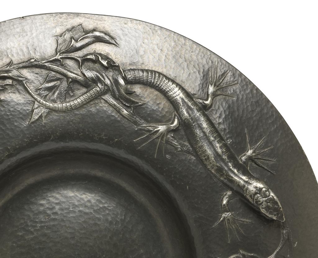 An image of Plate. Marks, Gilbert Leigh (British, 1861-1905). Decorated in relief with three lizards amid foliage. Circular with wide, downward curving rim, and small, deep well. Pewter, height, 2.8, cm, diameter, 23.5, cm, dated 1902. Arts and Crafts. Acquisition Credit: Given by Mrs J. Hull Grundy.