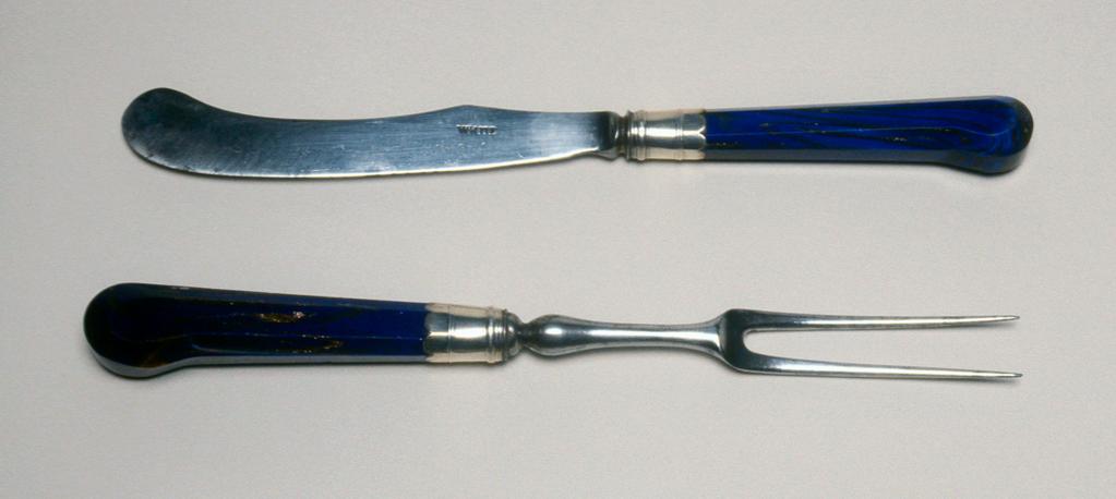 An image of Cutlery/Knife and Fork. White, Amos, cutler (English). Unknown handle maker, Italy, The Veneto. The knife has a steel scimitar-shaped blade with rounded tip; the handle is of blue aventurine glass which is flecked with bronze to resemble lapis lazuli. The facetted pistol grip handle has a silver ferrule embossed with two reeded borders and with an invected edge; the fork has two long steel tines on a baluster stem. The handle is similar to that of the knife. Glass, silver and steel, length, knife, 16.8 cm, length, fork, 14.7 cm, circa 1720-circa 1750. From slide: SL.8041.