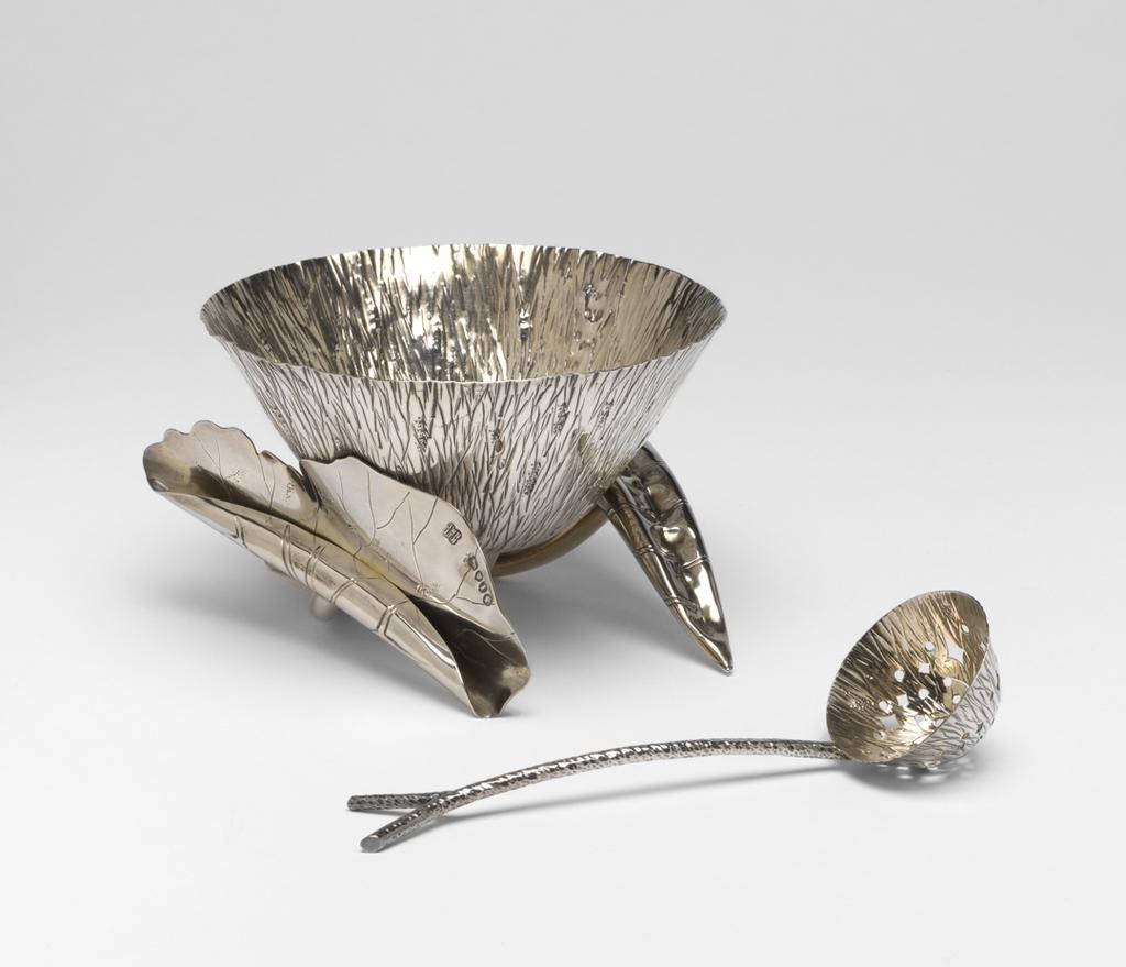 An image of Sugar bowl. Sugar sifter/spoon. Hukin, Jonathan Wilson, silversmith (British). Heath, Thomas, silversmith (British). Dresser, Christopher, designer, perhaps (British, 1834-1904). The bowl is in the form of a lotus flower with a lightly gilt interior, supported by a bent tubular stem, and two curled leaves with engraved veins and tubular stems branching out to right and left from beside the main stem. One leaf is completely curled, the other half open. The sifter spoon has a twig-shaped handle with forked terminal. It's bowl is of the same lotus flower form as the sugar bowl and it also lightly gilt; it is pierced with a pattern of lozenges and roundels. Silver, parcel-gilt, chased and engraved, height, bowl, 8.1 cm, varies, width, bowl, 12.4 cm, weight, bowl, 220 g, length, spoon, 14.9 cm, weight, spoon, 27 g, 1884-1885. Arts and Crafts. Production Note: The attribution of the design to Christopher Dresser is uncertain.
