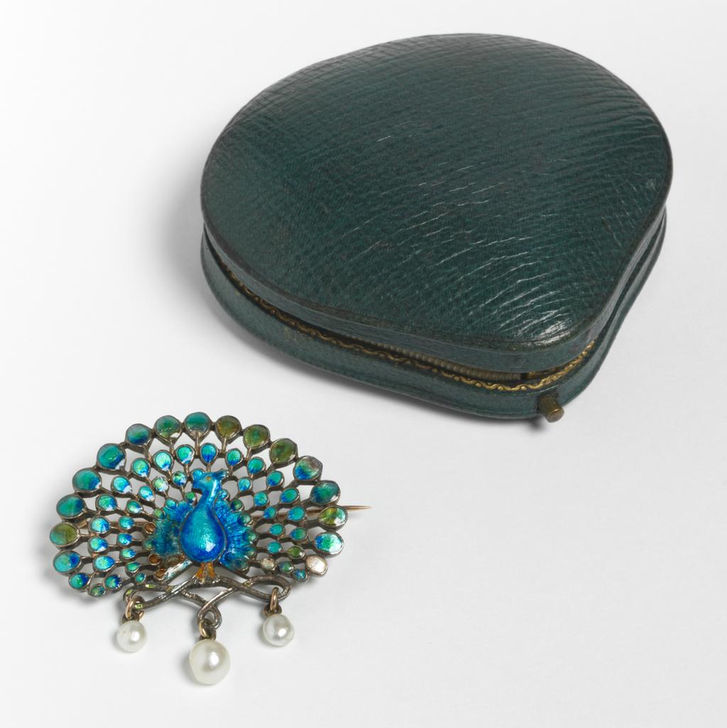 An image of Jewellery. Peacock brooch. Child & Child, London. In the shape of a peacock standing on three loops, from each of which is suspended a pearl drop. Pin-fastening across the back. In original dark turquoise leather case (A), lined with cream velvet and silk, the lid printed in gold 'CHILD & CHILD JEWELLERS/GOLD AND SILVERSMITHS/35 ALFRED PLACE WEST/QUEEN'S/GATE'. Gold, enamelled in blue, turquoise, yellow and green, with three pearl drops. Circa 1891-1899. Acquisition: given Mrs H. Hull Grundy.