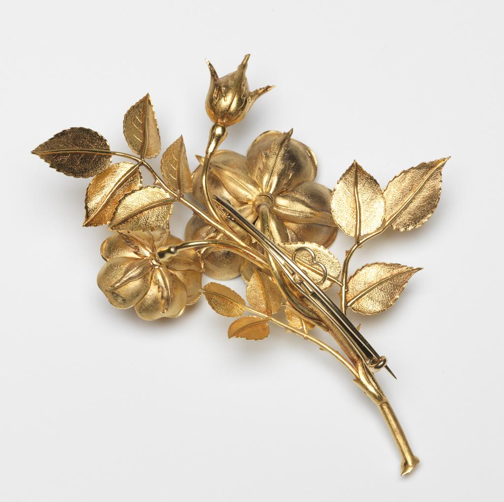 An image of Jewellery. Brooch. Hunt and Roskell, London. Gold, cast and chased in the shape of a spray of wild roses; detachable brooch-pin-fastening (A) screwed onto the back. Accompanied by a two-pronged pin (B) which converts the brooch into a hair ornament when screwed into the back in place of the pin-fastening. In rectangular maroon velvet case (C), the lid of which is lined with white silk and stamped in gold with the maker's name and address. The hair pin lies in a separate compartment in the base of the case. Height, brooch, 9.0 cm, width, brooch, 7.0 cm, length, pin, 12.1 cm, circa 1850. Acquisition Credit: Given by Mrs J. Hull Grundy.