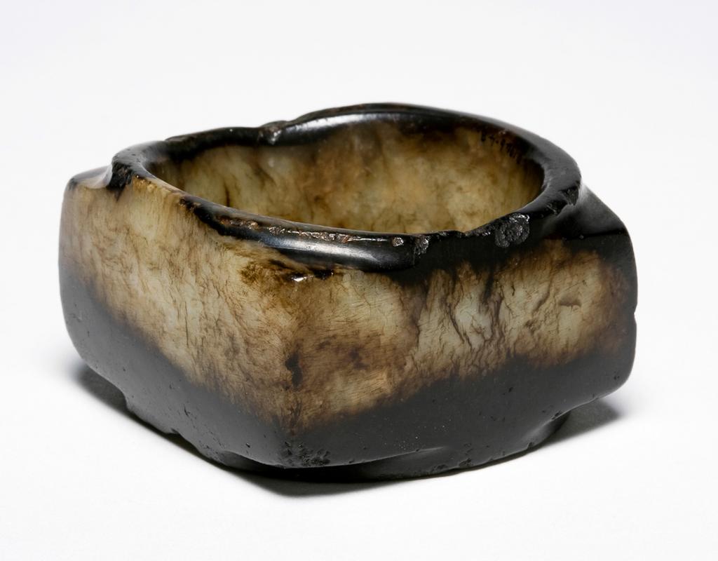 An image of Cong/Tube. Creamy white jade with dark veins, half of the body altered to a rich dark black colour. The central hole drilled from both ends and polished smooth on the inside. Nephrite, height 3.3 cm, length 5.9 cm, width 5.7 cm, 1050-771 BC. Chinese.