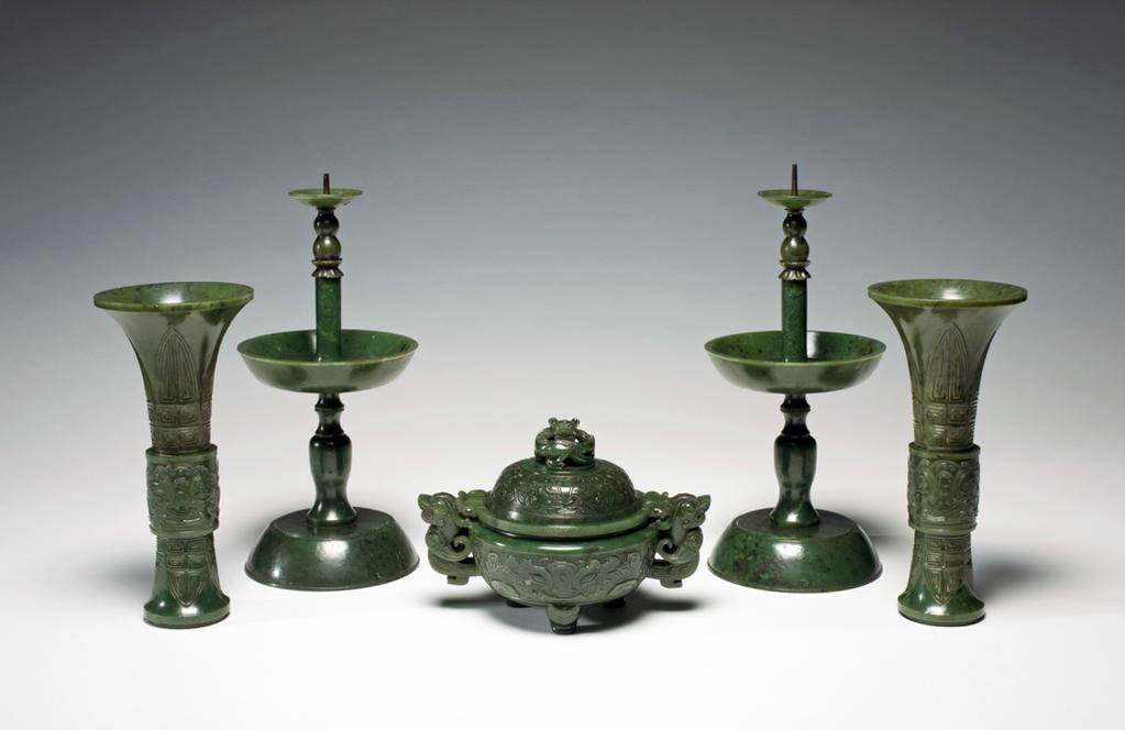 An image of Altar set of five pieces. Dark green with black spots; a Buddhist altar set of five pieces; two pricket candlesticks, two vases, and an incense burner. The two vases and incense burner are carved with ancient jade designs. The set are mounted on an elaborately carved wooden stand. Jasper, 1700-1800. Chinese.