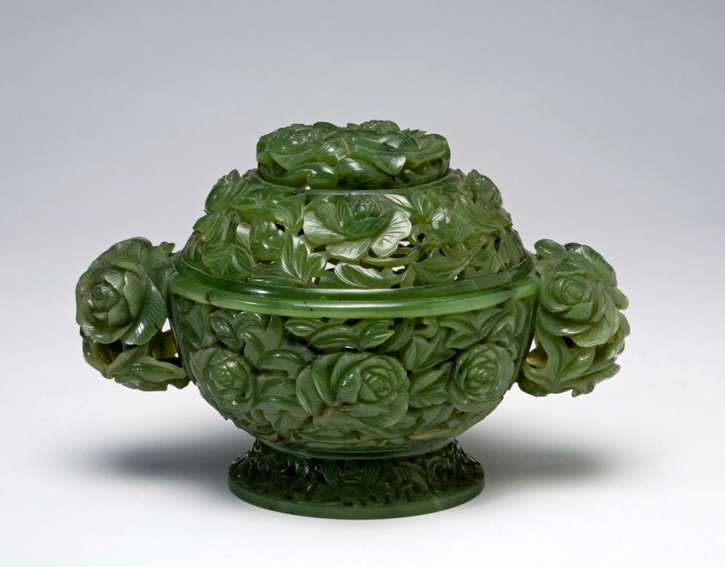 An image of Pomander. Dark spinach green jade, carved and pierced with full-blown peony flowers and foliage. The base flanked by two peony head handles and the domed cover surmounted by three openwork peonies. The openwork design suggests that it was used for non-burning incense or aromatic substances, such as dried flowers. Nephrite, height 9.8 cm, length, including handles, 15 cm, diameter 10.2 cm, 1736-1795 AD. Chinese.