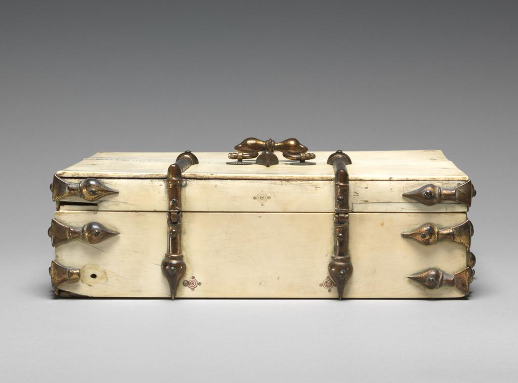 An image of Sculpture / Casket. Unknown Maker. Rectangular casket of ivory, lined with velvet. The gilded metal mounts have bulbous points with tapering ends. A gilt metal handle is placed in the centre of the lid and of two sides. Decoration consists of small engraved patterns of concentric circles around a dot with smaller circles at the cardinal points. They are placed around the edges of the box, mainly to mask the oval marks of the dowels. School/Style: Siculo-Arabic. Production Place: Sicily. Circa 1200-1330.