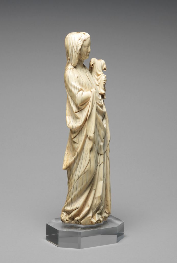 An image of Sculpture/Figure. The Virgin stands holding the Child in her left arm. Her tall figure sways backward, with the right knee breaking forward, and her head slightly tilted to the left. The smile is faint on the traditional oval face. Her mantle falls in broad soft folds. Ivory, carved, height, whole, 27.1 cm, width, whole, 8.0 cm, circa 1330-1370. Gothic, Medieval. French.