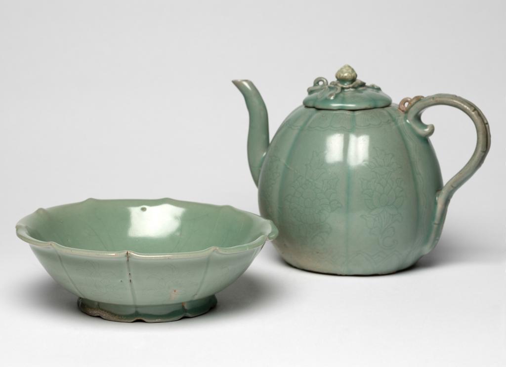 An image of Ewer and cover. Unknown pottery, Korea, North Cholla province. Puan-gun, Yuch'on-ri kilns or Kangjin-gun, Sadang-ri kilns. The ewer has an eight-lobed body, curved spout, and a handle carved to simulate bamboo, with a loop in the form of a lotus bud on top. The footring is very shallow. The eight-petalled lid has a (replaced) lotus-bud knob accompanied by applied stem and leaves. A band of petal panels is incised at the mouth and one of lotus petals at the base, each lobe shows a delicate spray of lotus, and a large lotus leaf is incised on the spout. The cover is incised with a classic-scroll border. The glaze is of pale bluish-green jade colour, thickly applied and glossy, and on the ewer partly discoloured. The ewer shows large uneven spur-marks near the footring and in the centre of the base. Stoneware, thrown, with parts attached, indented, incised and celadon-glazed. Height, whole, 18.3 cm, diameter, rim, 4.5 cm, diameter, foot, 9.8 cm, circa 1150-1200.  Koryo Dynasty. Related object: C.53-1984 basin.