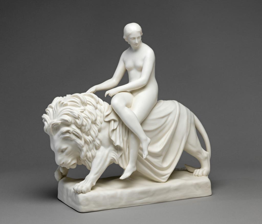 An image of Figure Group. Una and the Lion or Purity. Minton Factory, Stoke on Trent. Bell, John, modeller (British, 1811-1895). The figures are supported on a rectangular base with a flange round the outer edge underneath on which it rests. The lion is walking to the left and has its left front paw raised slightly, Its left back paw is forward and the right back paw is back. The tip of the tail rests on the ground. The lion is partly covered by a loose drape on which Una sits. She is nude and looks modestly downwards. Her right leg is crossed over her left and she holds a piece of the Lion's mane in her right hand. Parian porcelain, slip-cast, height, whole, 37.5 cm, length, whole, 37.8 cm, 1860. Victorian.