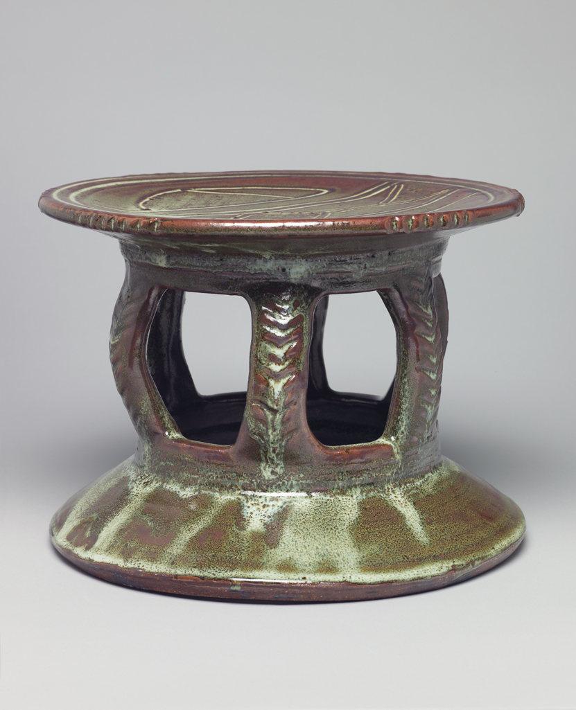 An image of Studio Ceramics. Stool. Cardew, Michael (British, 1901-1983). Stoneware drum seat of Abuja style. Supported by six ribs only, no central vase as in some examples. Incised chevrons on the ribs. Brown-green glaze with an abstract sgraffito design on the upper surface through to a white slip, presumably zircon. Before 1971. Acquisition: Dr John Shakeshaft Bequest.