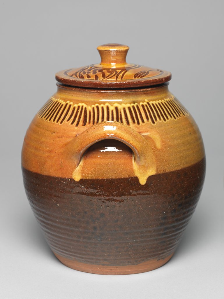 An image of Studio Ceramics. Earthenware slipware lidded storage jar with two handles. Cardew, Michael (British, 1901-1983). White slip on upper half and on lid, with decoration through the slip in the Cizhou style. With a clear yellow galena glaze overall, circa 1936. Acquisition: Dr John Shakeshaft Bequest.