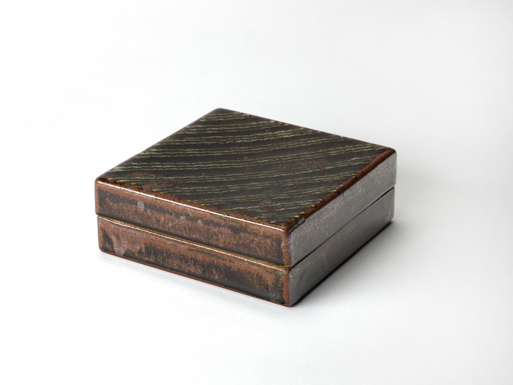 An image of Studio Ceramics. Box and cover. Hughes, Edward (British, 1953-2006). Square, with both halves of almost the same depth. Stoneware, slab-built in two parts, the interior coated with transparent, speckled grey-green glaze; the exterior with dark-brown and red-brown glaze; the cover trailed with diagonal stripes, and feathered. The base, the lower edge of the sides of the cover, and the upper edge of the sides of the box are unglazed. Height, whole, 6.2 cm ,width, base, 15.8 cm, length, base, 15.8 cm, 1989. Production Note: from the last firing at Renwick Pottery before the potter moved to Isel.