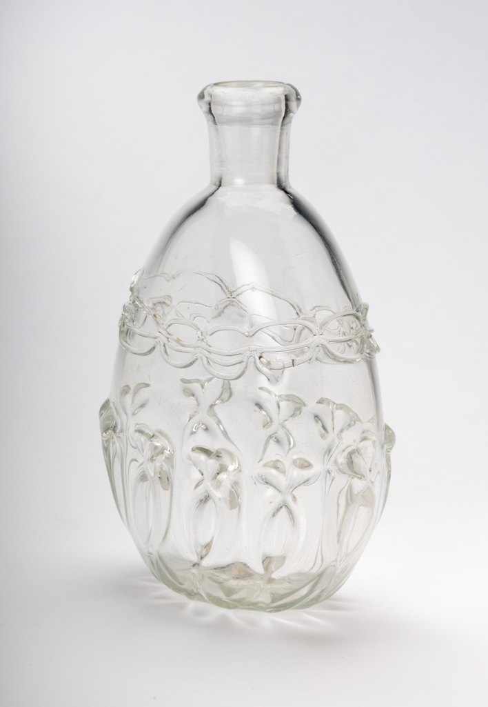 An image of Flask. Unidentified glasshouse, England. The flask is of flattened oval form with a cylindrical neck and inward folded mouth. The lower part is decorated with mould-blown ribbing which has been pincered to form ten oval outlines with pairs of bows (?) at the top. The shoulder has three bands of trailing tooled to form a double chain. Clear lead-glass, mould-blown, with applied pincered trailing, height, 13.6 cm, width, 9 cm, circa 1680-1710. Sir Ivor and Lady Batchelor Bequest through The Art Fund.