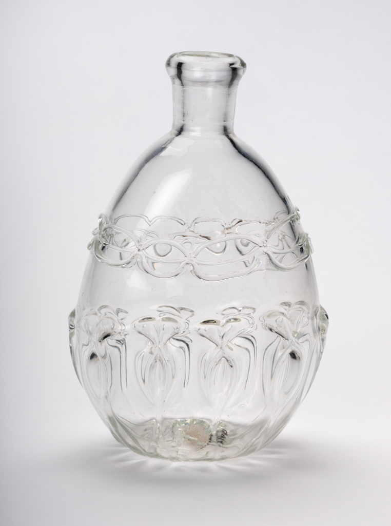 An image of Flask. Unidentified glasshouse, England. The flask is of flattened oval form with a cylindrical neck and inward folded mouth. The lower part is decorated with mould-blown ribbing which has been pincered to form ten oval outlines with pairs of bows (?) at the top. The shoulder has three bands of trailing tooled to form a double chain. Clear lead-glass, mould-blown, with applied pincered trailing, height, 13.6 cm, width, 9 cm, circa 1680-1710. Sir Ivor and Lady Batchelor Bequest through The Art Fund.
