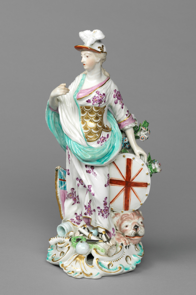 An image of Figure. Britannia. Derby Porcelain Factory, Derbyshire. William Duesbury & Co., proprietor. The base is approximately circular with a rococo scrolled and pierced front edge, and rises up at the back into a broad tree trunk with two branches bearing flowers and foliage on the figure’s left. Britannia stands with her left foot slightly advanced, her head turned a little to her right as she looks towards her raised right hand. Her left arm is a little behind her, the hand supporting an oval shield charged with red crosses of St George and St Andrew, which rests on the head of a lion. She has long, pale brown hair, tied back, and a cap with three white feathers at the front and a red underside to the peak. She wears a white dress with a puce floral pattern, pink cuffs, and pink drape round the neckline, a gilt scale cuirass, a white and turquoise shawl draped over her right shoulder and arm, and black sandals with a gold button on top. On the figure’s right a pink flag with a Union Jack in the top corner projects from the tree trunk. On the base there is a pale blue canon mouth, two pale blue canon balls of different sizes, a sword with a black scabbard with green wreath resting on it, and a white trumpet. The edge is picked out in turquoise and gold. Soft-paste porcelain, slip-cast, and painted overglaze in pale blue, turquoise, green, flesh pink, pink, puce, red, pale brown, and black enamels, and gilt. The unglazed underside has been ground flat, and has three patch marks, and a large circular central ventilation hole. Height, whole, 26 cm, width, whole, 12.8 cm, circa 1765. Rococo.
