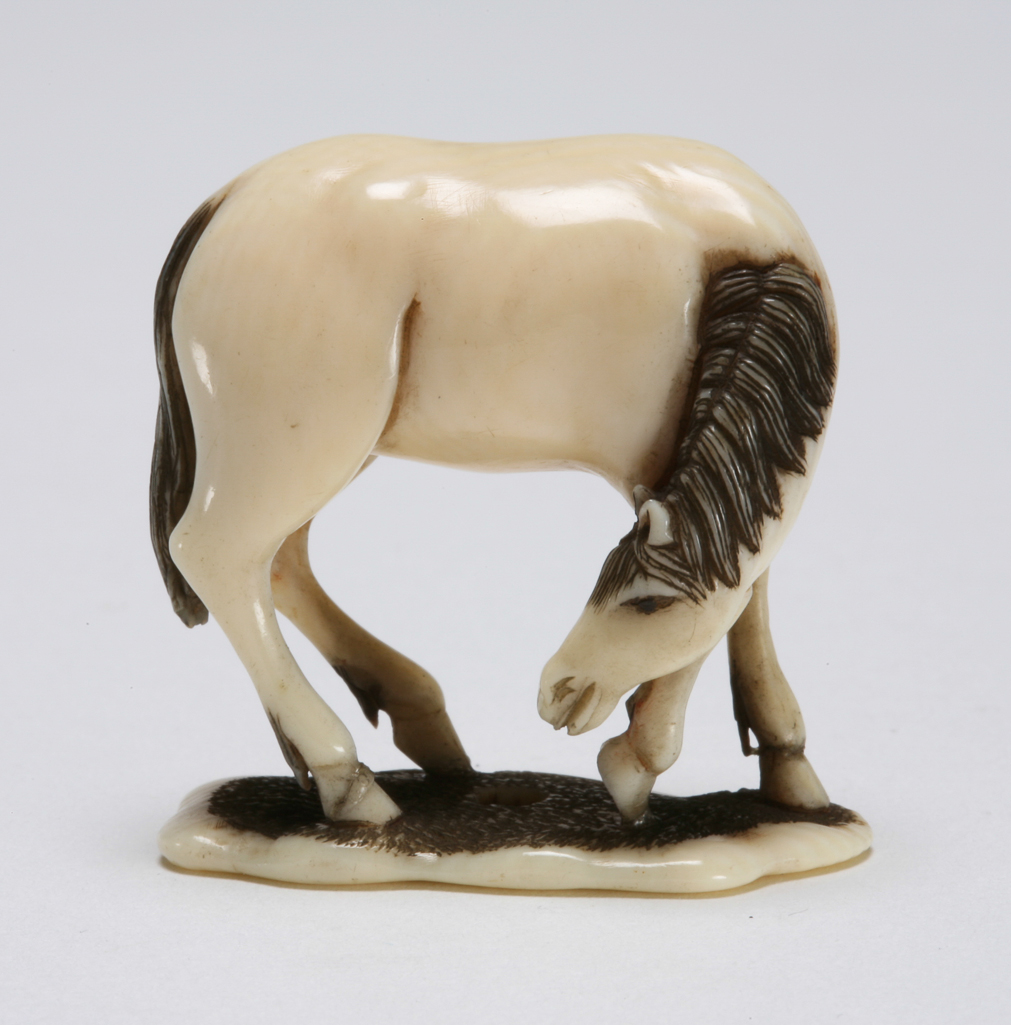 An image of Okimono. Unknown maker, Japan. A horse with lowered neck. Ivory with carved and stained detail, height 3.5 cm, width 3.5 cm. Japanese.