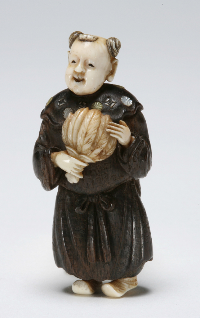 An image of Netsuke. Chinese boy, karako, holding a fan. Hōgyoku (Japanese). Wood and ivory, inlaid with mother of pearl, height 4.5 cm. Acquisition Credit: Marlay Bequest.