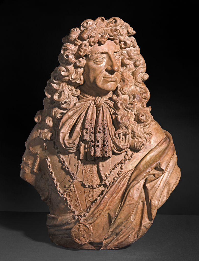 An image of Sculpture/Bust. King Charles II (1630-1685). Bushnell, John (British, c.1606-1701). Terracotta, height 78.5 cm, circa 1678. Baroque. The King's head is turned to the front, facing and looking half-right. He has a small moustache and a long, curling periwig, falling over both shoulders. He wears armour, with a double chain holding the Garter medallion of St George, a lace trimmed cravat tied in a bow, and a cloak draped over his left shoulder.