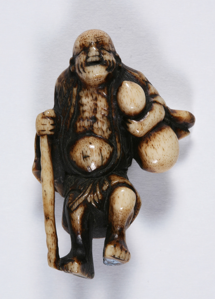 An image of Netsuke. Sennin Chokaro standing and holding a gourd and a walking stick. Unknown maker, Japan. Stag antler, carved, 1800-1900.