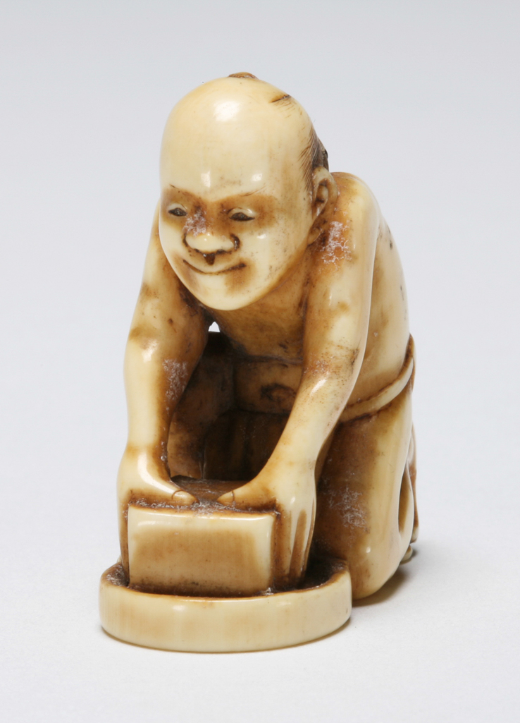 An image of Netsuke: katabori. Rat-catcher. Tomomitsu, Edo Period, 19th century, Japan. Crouching figure of a rat catcher with a cunning expression on his face, wearing a loin cloth and holding his box trap; the rat sits on his right shoulder. Natural himotoshi formed by his arms and legs. Ivory, carved and stained, height, whole, 3.7 cm, width, whole, 3.4 cm, circa 1800. Edo Period (1615-1868).