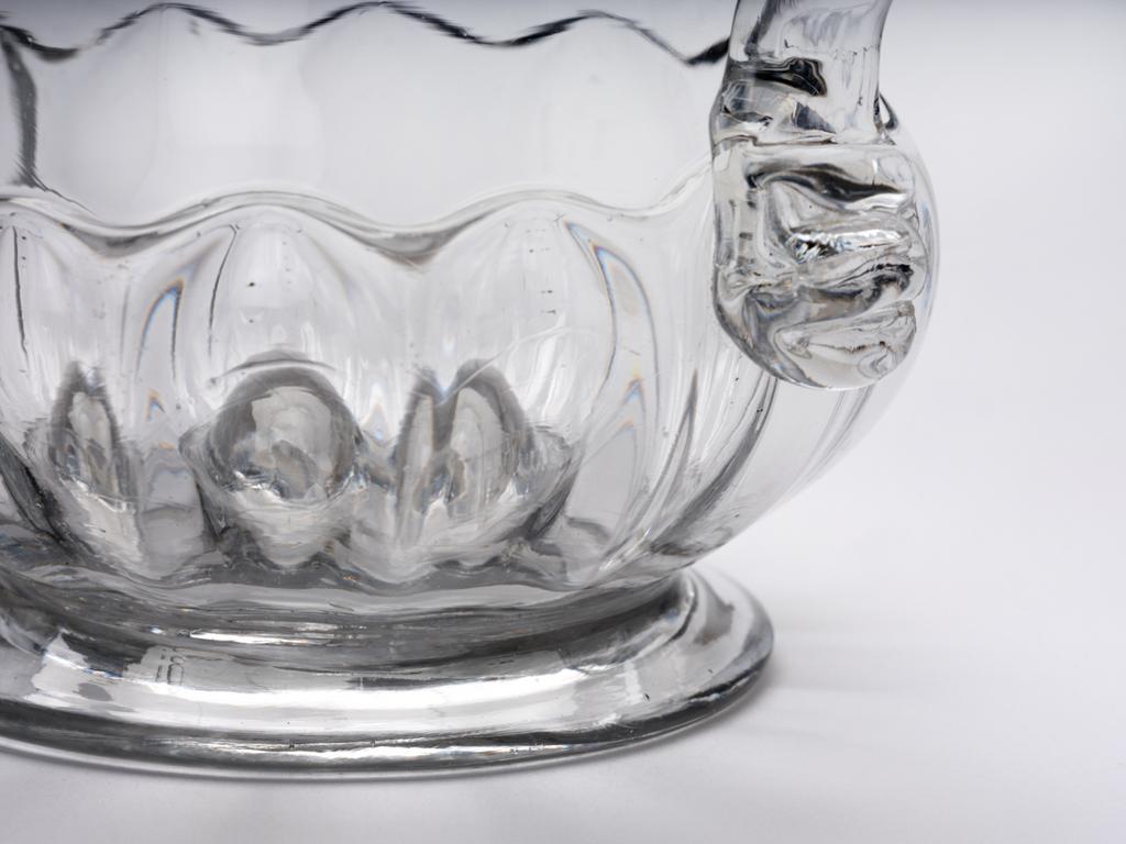 An image of Mug. Tankard. Unidentified English glasshouse. The waisted thistle-shaped tankard has mould-blown gadrooning on its lower part, and stands on a low foot. The handle is of D-section and has a folded kick at the lower end. Clear lead-glass blown and mould-blown. 1720. Baroque. Sir Ivor and Lady Batchelor Bequest through The Art Fund.