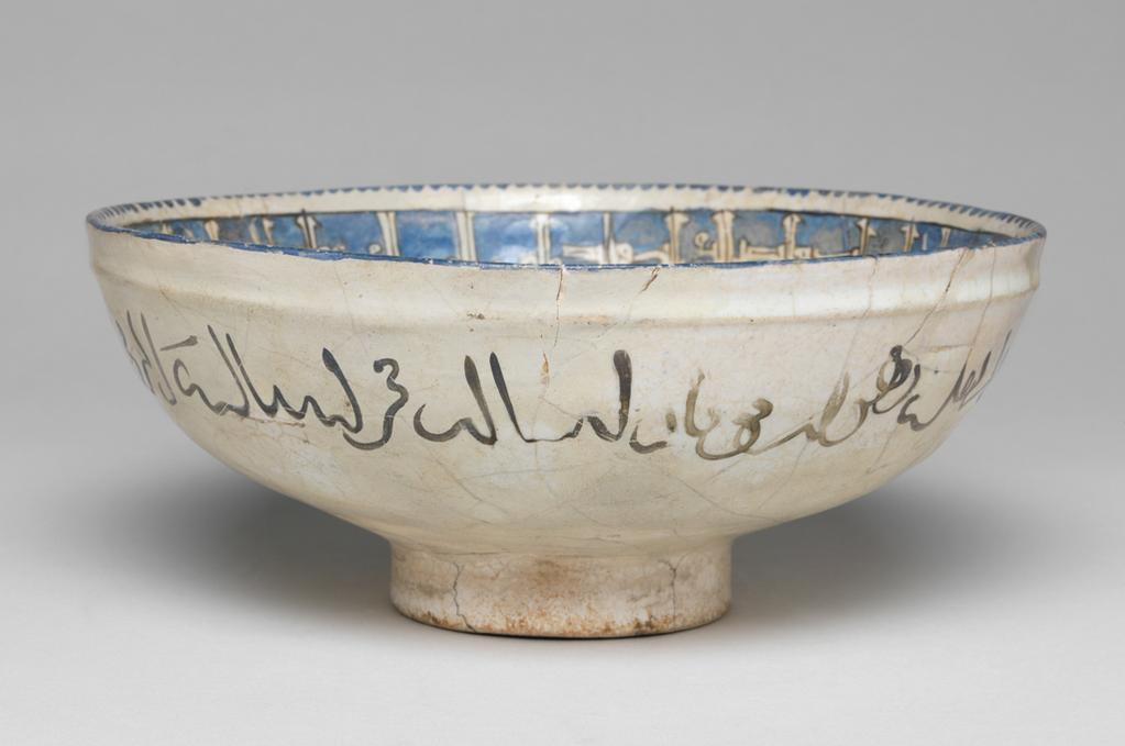 An image of Bowl. Islamic pottery, Minai. Unknown potter, central Asia, probably Kashan. Shape: hemispherical bowl with collared neck, sits on a low foot ring. Interior: the rim is painted with a blue dentilated pattern. On the neck and around the edge of the roundel, a kufic inscription is outlined in black and reserved in blue. On the body pairs of opposed, gesticulating male figures wear blue, purple or green patterned robes with gilding and red, purple or blue hats. Green tear-drop cartouche adorned with blue or red circles separate the pairs of figures. On the base, a mounted horseman, dressed in purple robes, rides a blue dappled horse and supports two hawks. Exterior: the rim is painted blue, on the neck a naskh inscription is painted in black. Glaze covers the exterior surface evenly except the underside of the foot ring. Fritware, wheel thrown, coated in a white glaze painted in six colours and gilded. Height, whole, 8 cm, diameter, rim, 18.8 cm, diameter, base, 6.8 cm, weight 336 g, circa 1170-circa 1220. Seljuk.