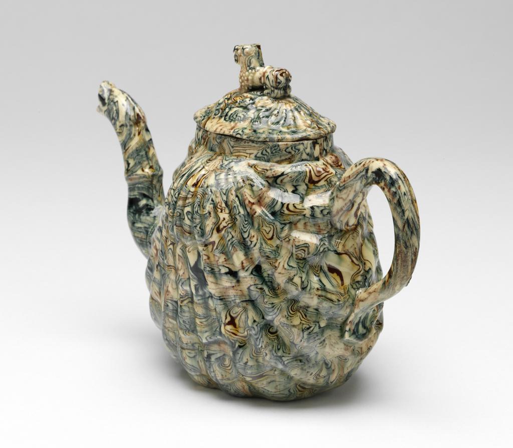 An image of Teapot and cover. Unidentified Staffordshire Pottery. The body is moulded on each side in the form of a pecten shell. The round loop handle flattens and has a slight kick at the base. The curved spout has a slight ridge half-way up and terminates in a serpent's head with an open mouth. The oval, slightly domed and fluted cover has a knob in the shape of a Buddhist lion. Cream, brown, and blue agateware, press-moulded, and lead-glazed overall except for a small area on the base. Height, whole, 13.0 cm, length, whole, 17.3 cm, 1750-1760. Rococo. Sir Ivor and Lady Batchelor Bequest.