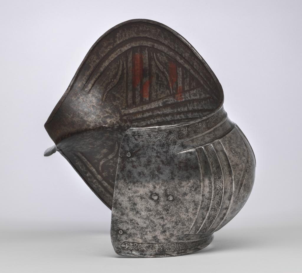 An image of Armour. Couter and lower cannon of a vambrace for the right arm, for parade use, with 'puffed-and-slashed' decoration in imitation of civilian costume. Production Place: South Germany. Helmschmied, Koloman (German, 1470/71-1532). The couter is formed of a single, large, shell-like plate, open at the rear and strongly shaped to the point of the elbow. Its outer edge is nearly straight. Its upper and lower edges are convex and converge at the inside of the elbow in a strong, medial pucker. The upper and lower edges have inward turns, roped with pairs of incised lines. The turns are each accompanied by a recessed border which is itself accompanied on the front by a flute separated from the border by a raised rib emphasised by a pair of incised lines. The boss over the elbow is enclosed by two groups of three flutes, each emphasised by pairs of incised lines, that converge to the inside of the elbow. Two vertical groups of such flutes decorate the front of the couter both above and below the boss, while three more decorate the boss itself. The broad bands intervening between these groups of flutes are decorated with slender, diagonal, slightly recurved, recessed 'slashes' in imitation of those found on contemporary civilian costume. The front and rear of the central boss are each fitted with a pair of horizontally-aligned rivets for the attachment of a missing pair of vertical internal leathers that formerly connected the couter to the upper and lower cannons of the vambrace. The outer end of the couter is filled with a pair of widely-spaced, externally-flush rivets for the attachment of a missing bifurcated strap that terminated in a buckle to receive the missing strap that was formerly retained internally by a brass-capped, round-headed rivet and octagonal internal washer located just to the inside of the medial pucker, and passed around the rear of the elbow. The lower cannon is of tubular form, cut away in a concave curve towards the inside of the elbow, and constri