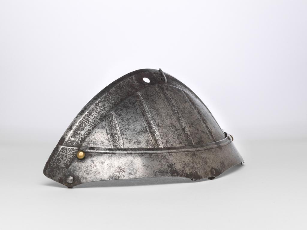An image of Armour. Top two lames of a spaudler for the right shoulder, for parade use, with 'puffed-and-slashed' decoration in imitation of civilian costume. Production Place: South Germany. Helmschmied, Koloman, armourer, possibly (German, 1470/71-1532). Consisting of two upward-overlapping lames of which the first is considerably deeper than the second and has a convex upper edge running into the lateral edges of the latter. This edge has a plain, partial inward turn accompanied by a recessed border decorated with an etched 'candelabrum' design on a plain, blackened ground. The first lame is decorated below this border with five, slender, vertical 'slashes' in imitation of those found on contemporary civilian costume. The upper edge of the second lame has a plain, partial, inward turn between the main borders at its outer ends. The lames were formerly connected to one another and to successive lames by brass-capped, round-headed rivets with irregular, internal washers at the rear, and by internal leathers secured to each lame by pairs of externally-flush rivets at the front and centre. All the rivets are preserved, but the rear rivet of the second lame lacks its brass cap. Both internal leathers are now missing.  The inner end of the second lame is fitted with a decorative, brass-capped, round-headed rivet, occupying a construction-hole that aligns with the outer pair of rivets that formerly attached the front leather to the first lame. The apex of the first lame is pierced with a pair of circular lace-holes to attach it to the collar. The lames are bright with patches of medium to heavy patination overall. Hammered, shaped, riveted, with a recessed border and etched decoration on a blackened ground. Height, whole, 9.8 cm, maximum, width, whole, 18.3 cm, maximum, depth, whole, 6.5 cm, maximum, weight, whole, 0.097 kg, c. 1520. Provenance: From the armoury of the Princes Radziwill, Castle of Niescwiez, Poland.