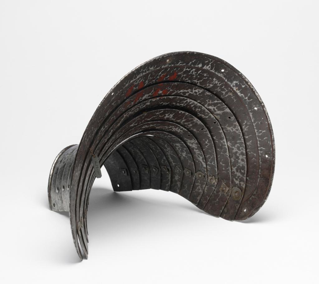 An image of M.9-1945: Armour. Defence for the left foreleg of a horse, for heavy cavalry use. Unknown production, Germany. Formed of twelve downward-overlapping lames curved to the front of the horse's upper foreleg and shoulder, and increasing in width to its upper end. The upper edge of the top lame is slightly convex with gently rounded corners. It has a file-roped inward turn accompanied by a recessed border containing nine holes for lining-rivets, of which six are occupied by externally-flush rivets. The lower edge of the bottom lame also has a file-roped inward turn. The outer ends of the lame on each are fitted with externally-flush rivets that formerly served to secure a strap around the rear of the horse's leg. The first to eleventh lames have bevelled outer edges. The lames are connected to one another at their outer ends by externally-flush sliding-rivets. The lames were further connected to one another by a pair of internal leathers located a short distance within the sliding-rivets. The leathers were attached to each lame by single externally-flush rivets. The rivets for the outer leather are preserved in the ninth to twelfth lames, and for the inner leather, in the eighth and ninth lames. The leg-defence has a ' black from the hammer' finish, now much worn, particularly at the centre of its lower half. Steel, hammered, shaped, riveted, with file-roped, recessed border and bevelled decoration. Height, whole, 25.5 cm, maximum, width, whole, 29.1 cm, maximum, depth, whole, 22.1 cm, maximum, weight, whole, 1.02 kg, circa 1550. Provenance: From the armoury of the Princes Radziwill, Castle of Niescwiez, Poland. Notes: forming a pair or near pair to M.14-1947. M.14-1947: Armour. Leg-defence for the right foreleg of a horse. Unknown production, Germany. Formed of twelve downward-overlapping lames curved to the front of the horse's upper foreleg and shoulder, and increasing in width to its upper end. The upper edge of the top lame is slightly convex with gently rounded c