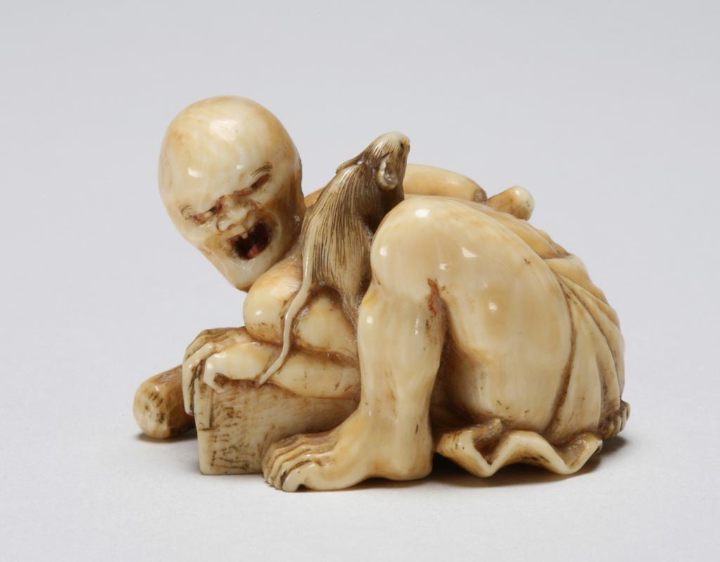 An image of Netsuke: katabori: Rat catcher. Masakazu, Edo Period, 19th century, Japan. Figure of an angry rat catcher half-nude crouching over a grain-measure holding a large club in his right hand and looking at the rat escaping over his left shoulder. The rat with finely incised details and black eyes, the man with a shaven head and his hair scraped into a bun; his tongue and eyes are tinted red. Himotoshi through the back of the grain-measure. Ivory, finely carved, incised and stained, height, whole, 2.6 cm, width, whole, 3.7 cm, circa 1800-1868. Edo Period (1615-1868).