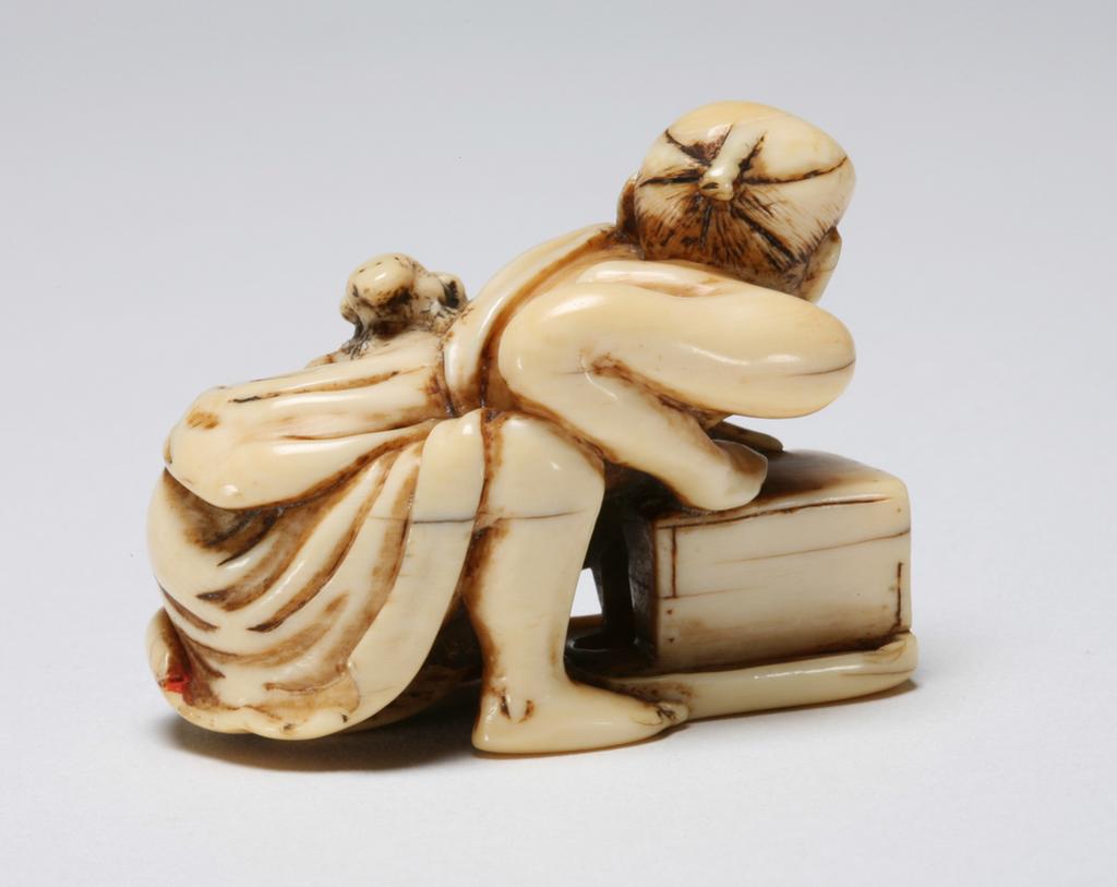 An image of Netsuke. Katabori. Rat-catcher. Unknown maker, Japan. Figure of a robed rat-catcher crouching over his grain-measure and grimacing as the rat scampers over his back. Incised and stained details. Himotoshi through the back of the grain-measure. Ivory, carved, incised and stained, height, whole, 3.8 cm, width, whole, 4.5 cm, circa 1800-1868. Edo Period (1615-1868).