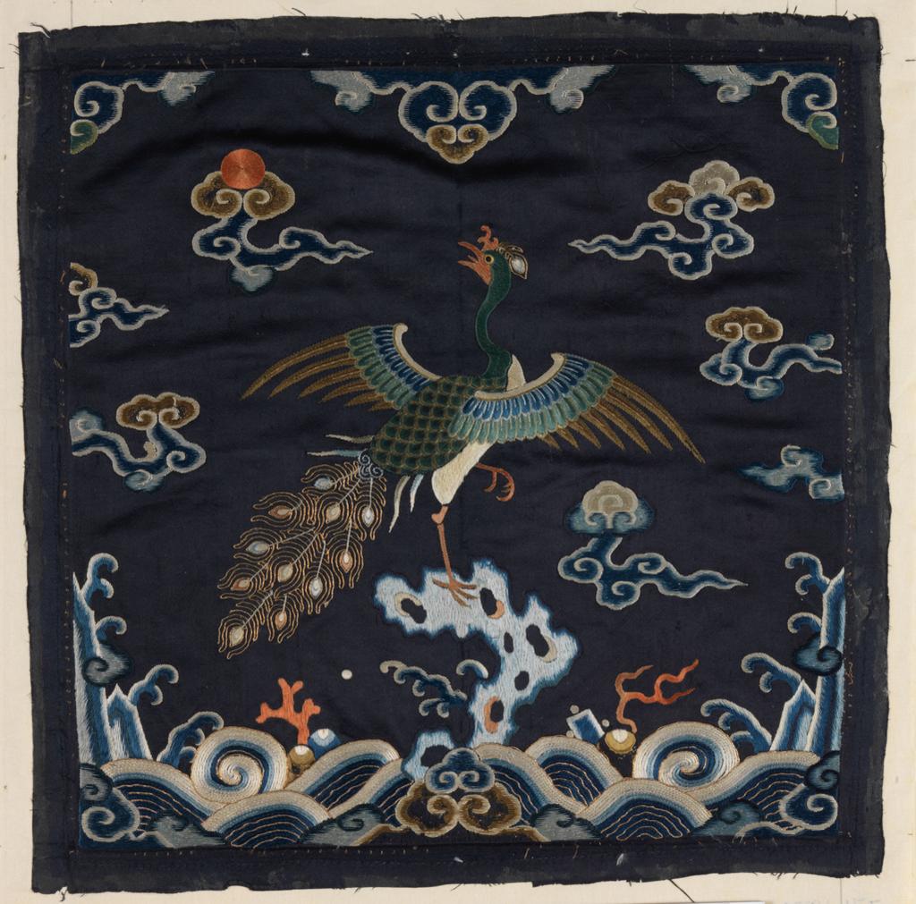 An image of Textiles. Mandarin Square. Unknown maker, China. Peacock feather on pheasant's head. Satin stitch, stem stitch, couched stitch, hem stitch, and laid work. Peacock perched on rock against a background of sky, clouds and waves, set in a wave and mountain border, with lucky symbols, clouds and a red sun above. Silk and metallic embroidery on satin - blues, greens, beige, white, red and gold. Length, whole, 29 cm, width, whole, 28.5 cm, circa 1700-circa 1799. Chinese. Acquisition Credit: Given by Mrs. Soame Jenyns, in accordance with the wishes of her late husband, Soame Jenyns.
