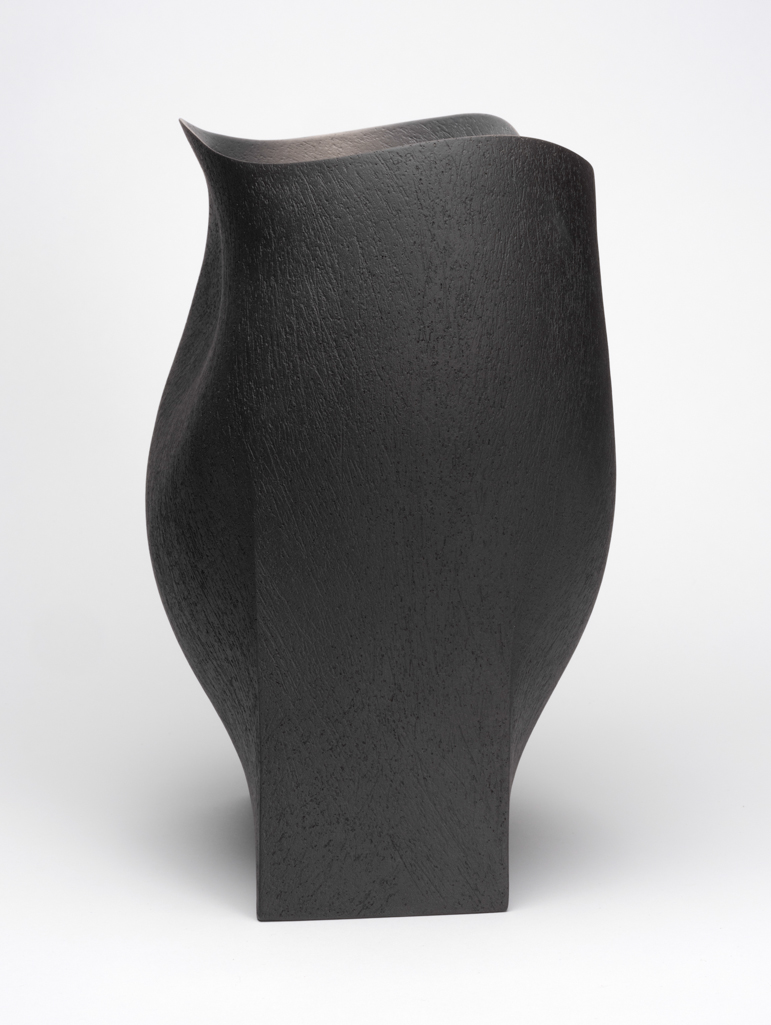 An image of Studio Ceramics. Undulating Vessel. Hanna, Ashraf (b. 1967, Egypt). Hand-built raku body clay coated with near-black slip. Hand built clay vessel, rising from a sharply pointed rectangular base. The sides flat at the base, rising into a softer curving form with a bulge on one side and a large dimple on the other, one slightly lower than the other giving a listing appearance. Undulating rim. Coated with near black slip and finely textured inside and out. Underside flat. Height 33 cm, width 30.5 cm, depth 20.5 cm, 2018. Gift of Nicholas and Judith Goodison through the Art Fund.
