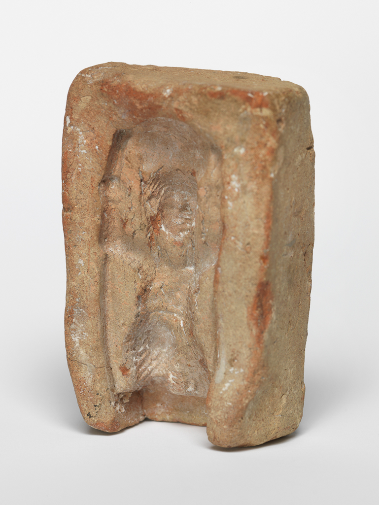 An image of Equipment/Mould. Shu, kneeling, holding sun disk above head. Production Place/Find Spot: Egypt. Length, design, 0.038 m.