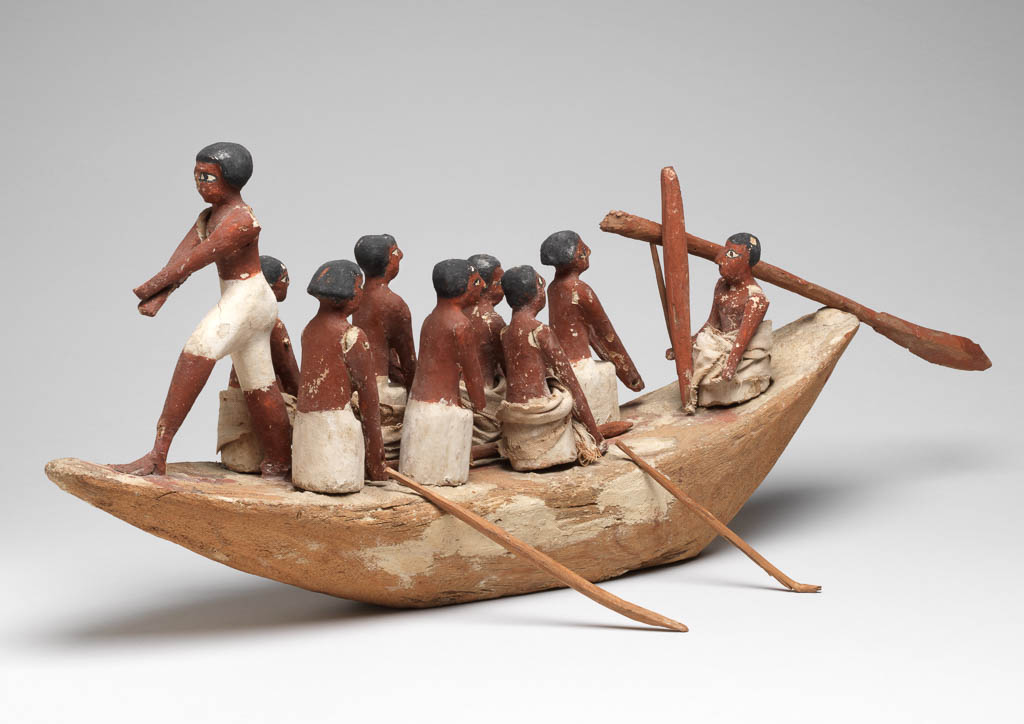 An image of Model Boat. Wooden model of a rowing boat with seven oarsmen (one missing at the front); a look-out on the prow; and a stroke caller (cox) in the bow. He sits beside a rudder-oar. The figures have white painted kilts and red-brown flesh. Some figures have real linen loin cloths. Production Place: Egypt. Find Spot: Tomb of Khety, tomb 366 (Beni Hasan), Egypt. Painted wood, linen, height, 25 cm, length 59 cm, width 12 cm, circa 2010-circa 1950 B.C. 12th Dynasty, Middle Kingdom.