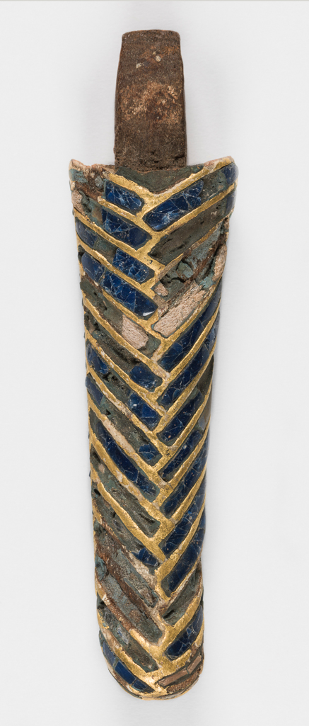 An image of Funerary equipment. Coffin fragment. Production Place: Egypt. Find Spot: Karnak, Egypt. Wooden beard from a New Kingdom coffin, inlaid with blue glass and detailed with gold leaf. Length 16.5 cm,1550-1070 B.C. New Kingdom.