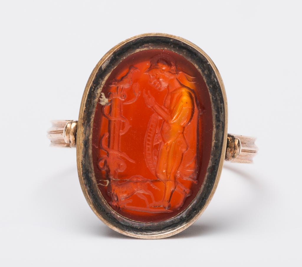 An image of Engraved Gems/Ringstone. Profile of a nude young warrior wearing only a helmet and chlamys, holding a shield. To his left stands a column entwined by a serpent on top of which sits a bird. Intaglio cutting, red-brown cornelian, height 15, mm, width 11 mm, depth 4 mm, circa 200- circa 100 B.C. Roman Republican.