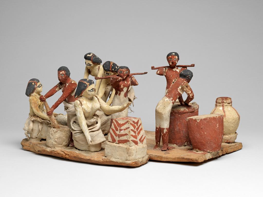 An image of Model Workshop. Wooden model of a brewing and baking workshop; two women grounding flour, one woman sifting flour, a man mixing dough, a woman by an oven, a man mashing beer, two men with yokes carrying vessels (supplied by E.172a-b.1903), two large vessels. Wood coated in plaster and painted red-brown, black, white, and pale yellow (women's flesh). The women and one man still have cloth garments. Production Place: Egypt. Find Spot: Tomb of Khety Beni Hasan; tomb 366. Wood, plaster and linen, painted, height 18.5 cm, length 41.4 cm, width 29.7 cm, circa 2010- circa 1950 B.C. Twelfth Dynasty; Middle Kingdom.