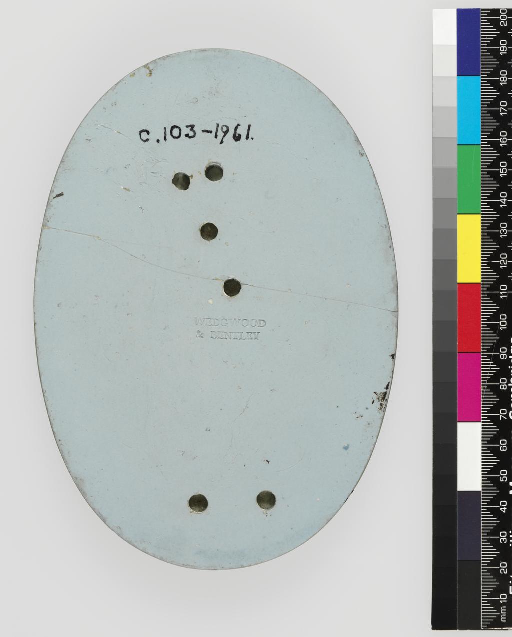 An image of Plaque of Apollo Musagetes. Wedgwood & Bentley, Staffordshire. Oval, the god stands on a projecting base, resting his left elbow on his lyre which stands upright on a tripod stand. There are two holes in the reverse behind the base, and four behind the figure. Jasper, pale bluish-grey with darker blue surface and press-moulded and applied white relief, height, whole, 16.7 cm, width, whole, 11.7 cm,  circa 1775- 1780. Neoclassical. Production Note: This Apollo from a set of Apollo and the Muses is probably the one partly supplied by Flaxman Senior in March 1775: Apollo, Melpomene, Thalia and Terpsichore, Euterpe.
