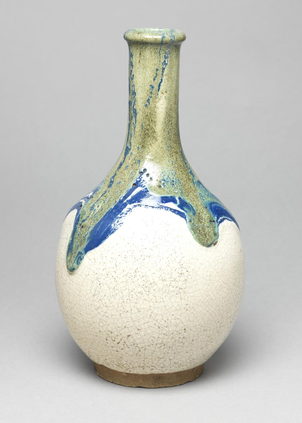 An image of Japanese pottery. Sake bottle. Unknown pottery, perhaps, Japan, Narita. Sake bottle of globular form with long neck. Buff body, thrown and turned. Cream glaze, the neck and shoulders covered with pours in blue and green. Heavy pitting visible. Stoneware, glazed, height 25.30 cm, diameter, rim, 4.30 cm, diameter, bottle, 14.10 cm, diameter, base, 8.20 cm, circa 1875-circa 1925. Meiji Period (1868-1912).
