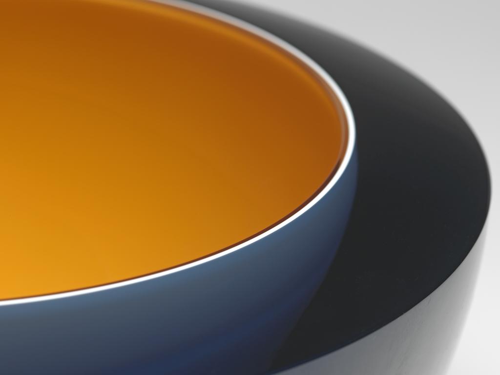 An image of Studio Glass; Contemporary Craft. Bowl with 'floating bowl'. Woodman, Rachael (British, b. 1957). Hemispherical with bevelled top edge, and a small circular base. A dark yellow bowl is cased in a thin layer of white, and a wider layer of translucent dark blue glass, which has been ground away on the base to reveal the white layer. Dark yellow glass, blown and cased in white and blue glass, with bevelled top edge, height, whole, 9.9 cm, diameter, whole, 18.6 cm, dated 1995. Gift of Nicholas and Judith Goodison through the National Art Collections Fund.