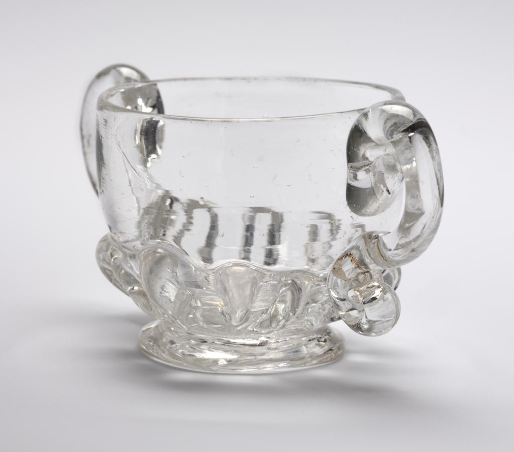 An image of Miniature two-handled cup. Loving cup. Unidentified glasshouse, England. Clear lead-glass with gadrooned lower part and two S-shaped handles, height, whole, 3 cm, width, whole, 6.7 cm, 1690-1720. Baroque. Sir Ivor and Lady Batchelor Bequest through The Art Fund.